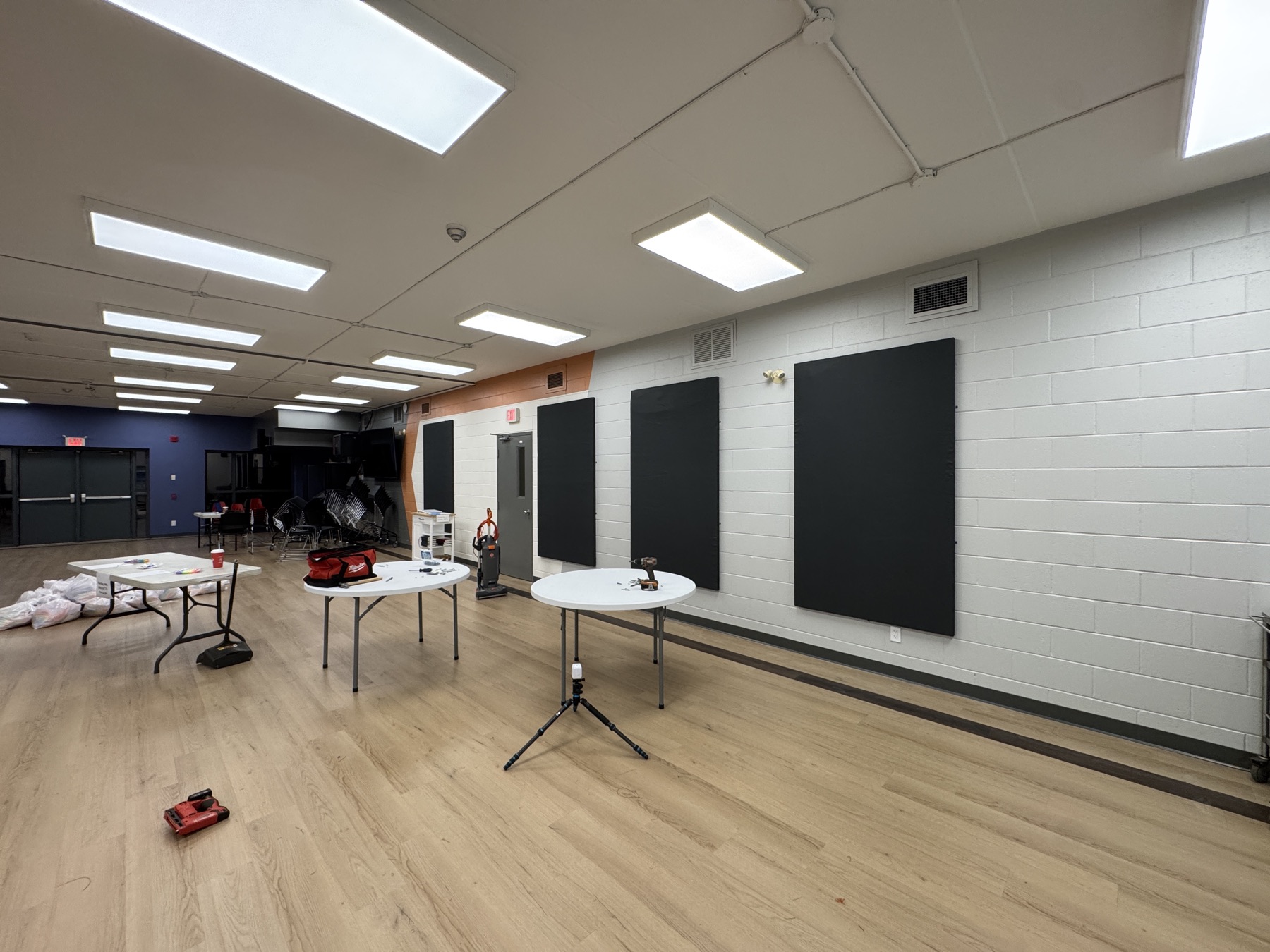 The church hall during installation: re-covered acoustic panels along the long block wall, with tables and tools on the floor