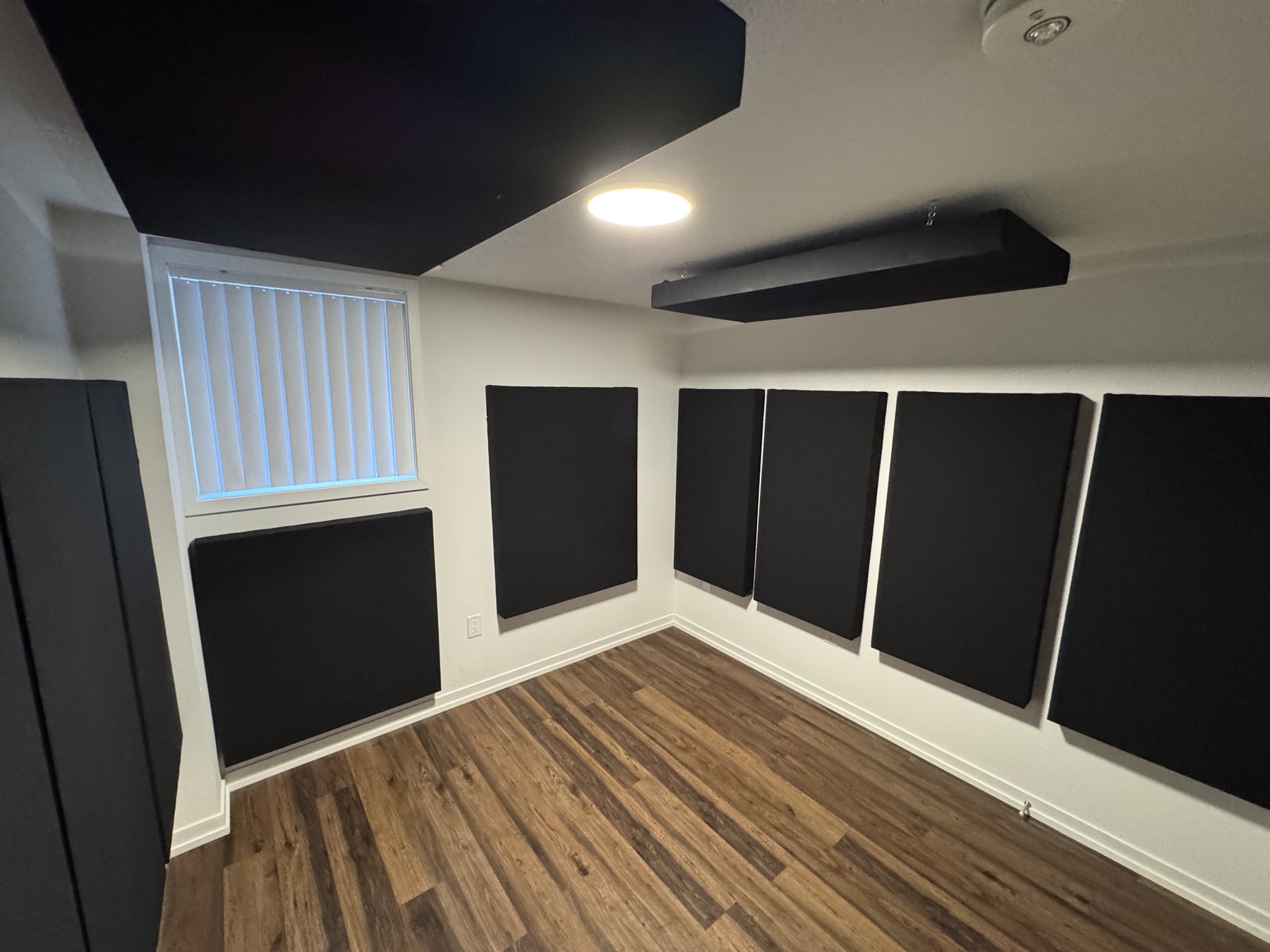 The studio from the other side: black acoustic panels under and beside the window, along the side wall, with a suspended ceiling cloud overhead