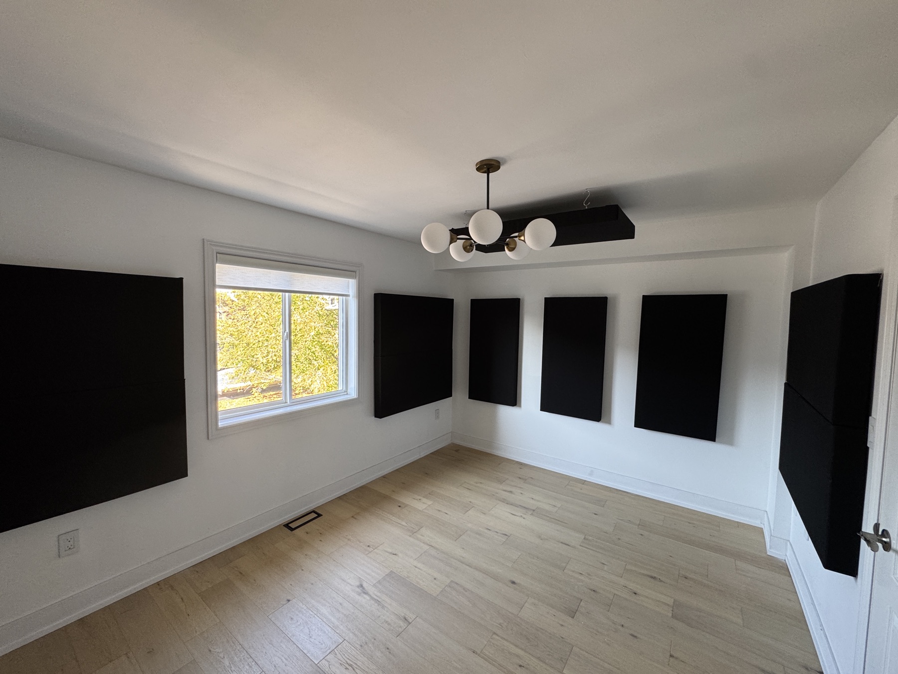 The voice-over room from the other side: black acoustic panels spaced along white walls around the window, above light wood flooring